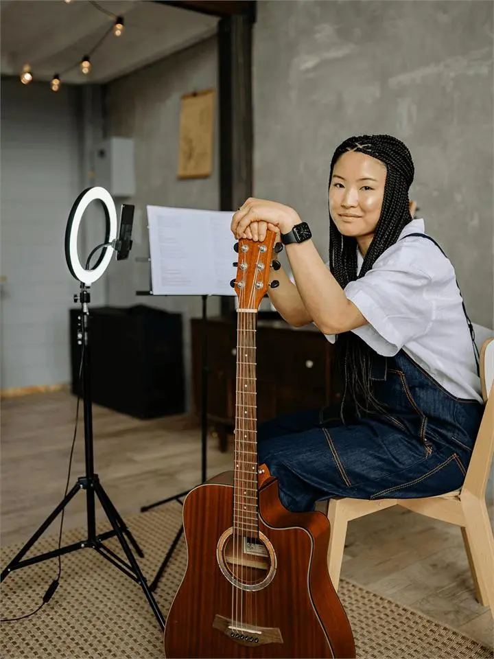 A smiling content creator with a guitar beside a ring light and music stand
