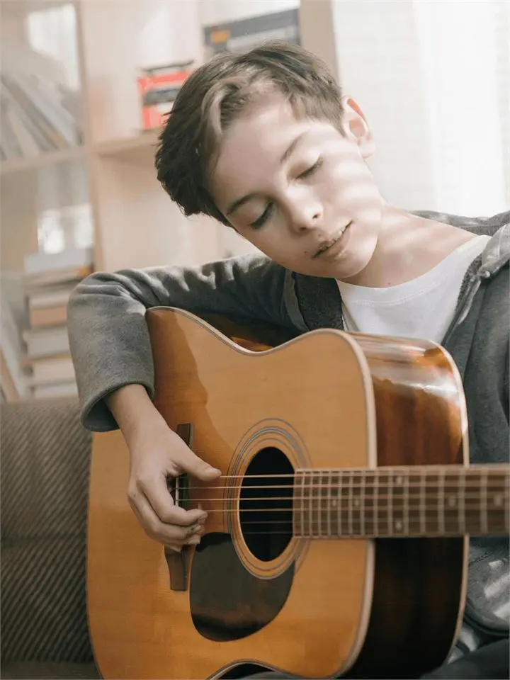 A teenager playing an acoustic guitar with his eyes closed