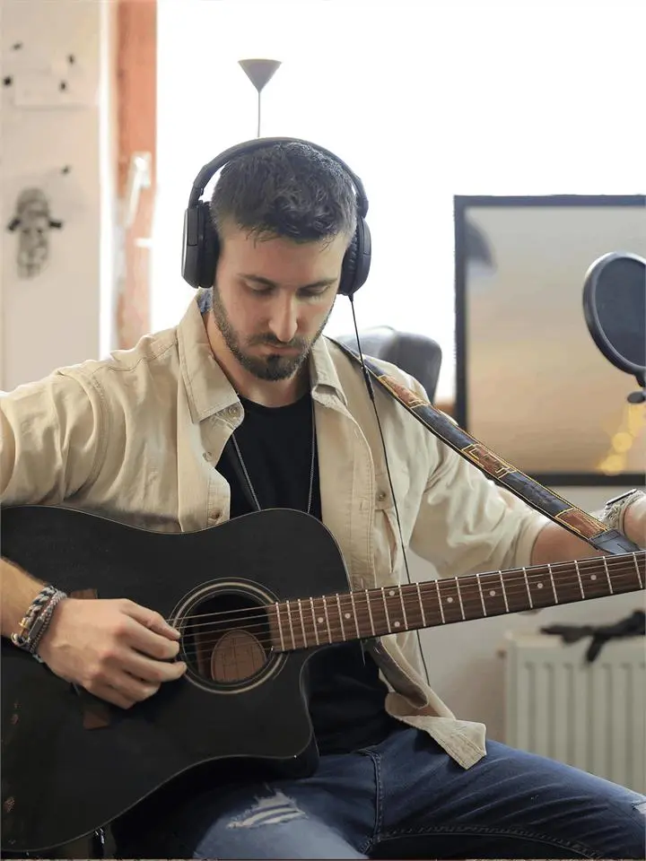 A man with headphones playing an acoustic guitar at home