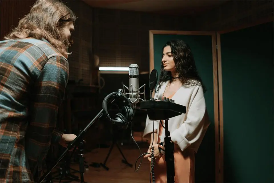A singer recording vocals at a condenser microphone in a studio booth