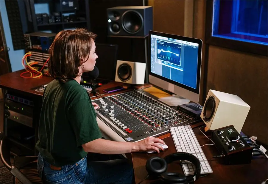 A person working at a recording studio mixing desk with monitor speakers